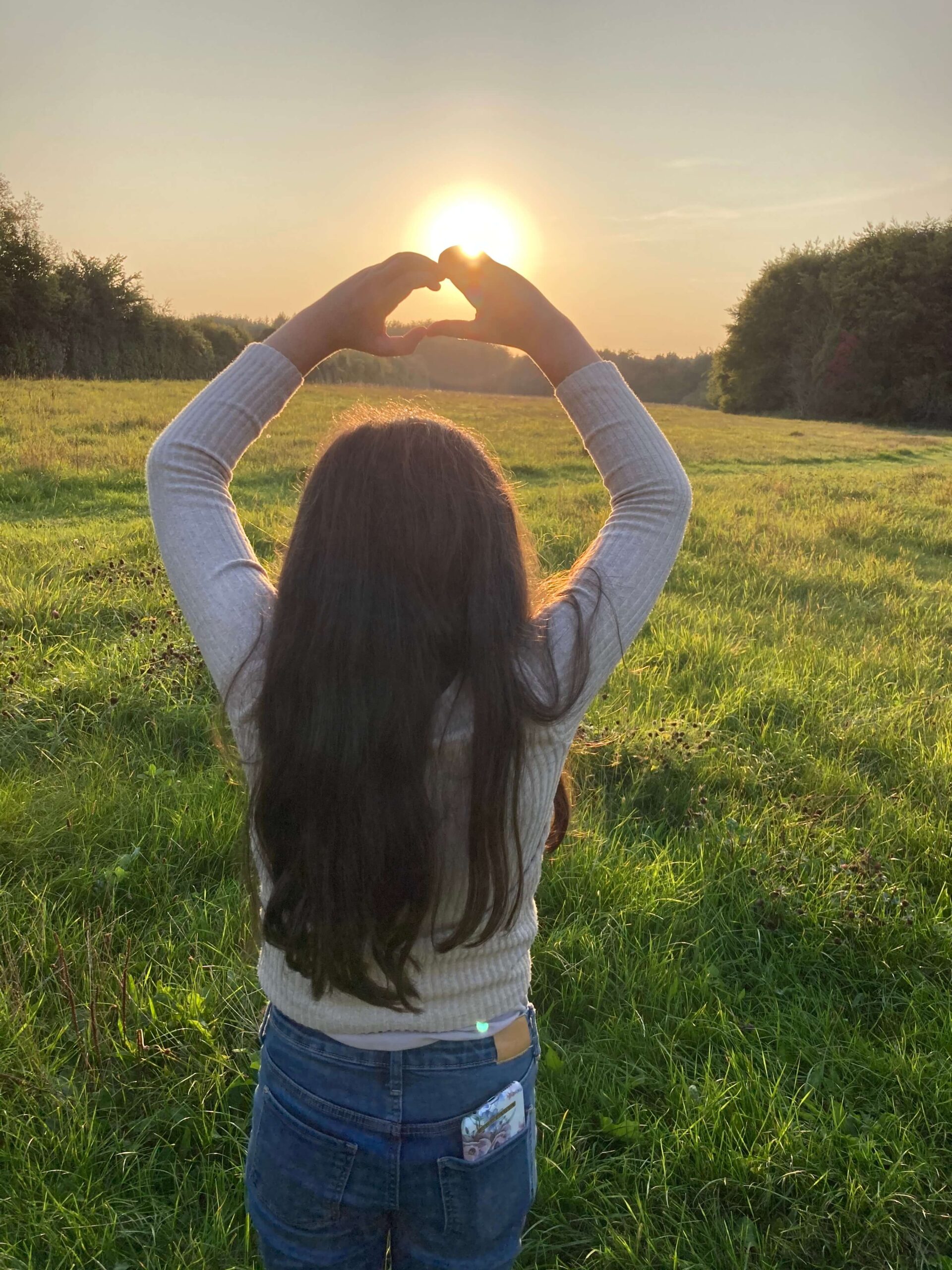 Pige danner hjerte med hænderne mod solen – symbol på håb og lys hos Familieløft